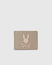 The Psycho Bunny MENS LEATHER WALLET - B6A868D200, featured on a plain background, displays an embossed rabbit's head with crossed bones. This beige wallet offers a minimalist and stylish design for those who value refined craftsmanship.