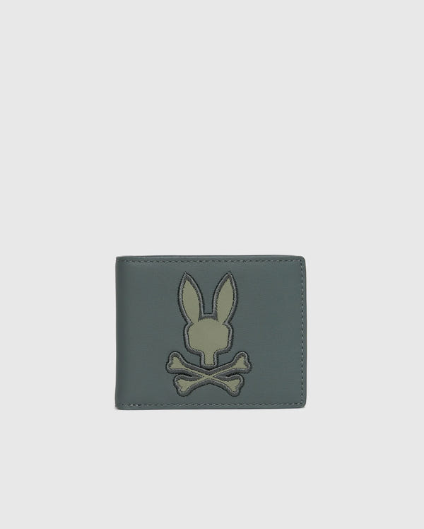 Introducing the MENS WORDMARK LEATHER WALLET - B6A868D200 by Psycho Bunny, a stylish accessory for men. This trendy green leather wallet showcases an embroidered rabbit head above crossbones on the front, set against a sleek white background.