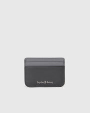The MENS LEATHER CARD CASE - B6A869D200 from Psycho Bunny is a sleek black rectangular holder made of premium leather, featuring two visible slots. It showcases the iconic "Psycho Bunny" logo and a small white bunny illustration on the bottom, set against a plain white background.