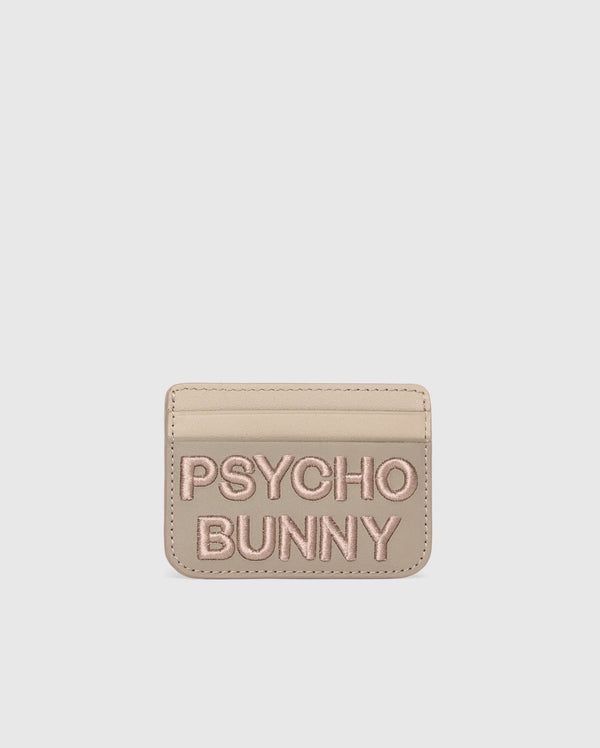 A premium beige leather cardholder features "PSYCHO BUNNY" embroidered in pink on the front. The minimalist MENS LEATHER CARD CASE - B6A869D200 by Psycho Bunny offers style and simplicity, set against a plain white background.