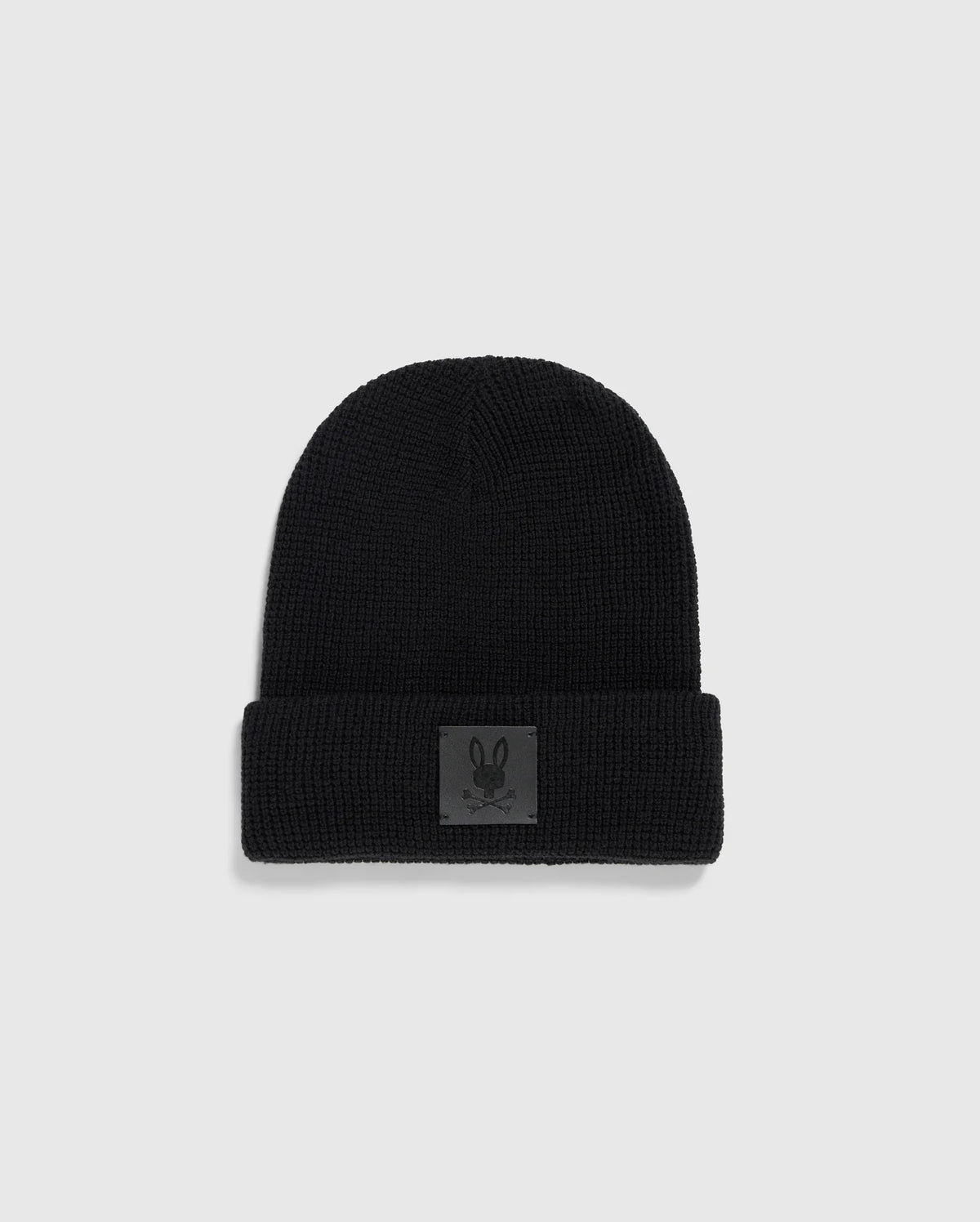 The Psycho Bunny MENS WAFFLE BEANIE - B6A873D200, crafted in black cotton knit with a folded brim, displays a small patch featuring a minimalist rabbit graphic. This winter knit hat is showcased against a light gray background.