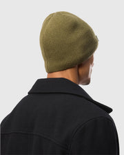 A person is shown from behind against a plain light background, wearing a Psycho Bunny MENS SPORT BEANIE - B6A874D200 in green knit along with a dark coat.