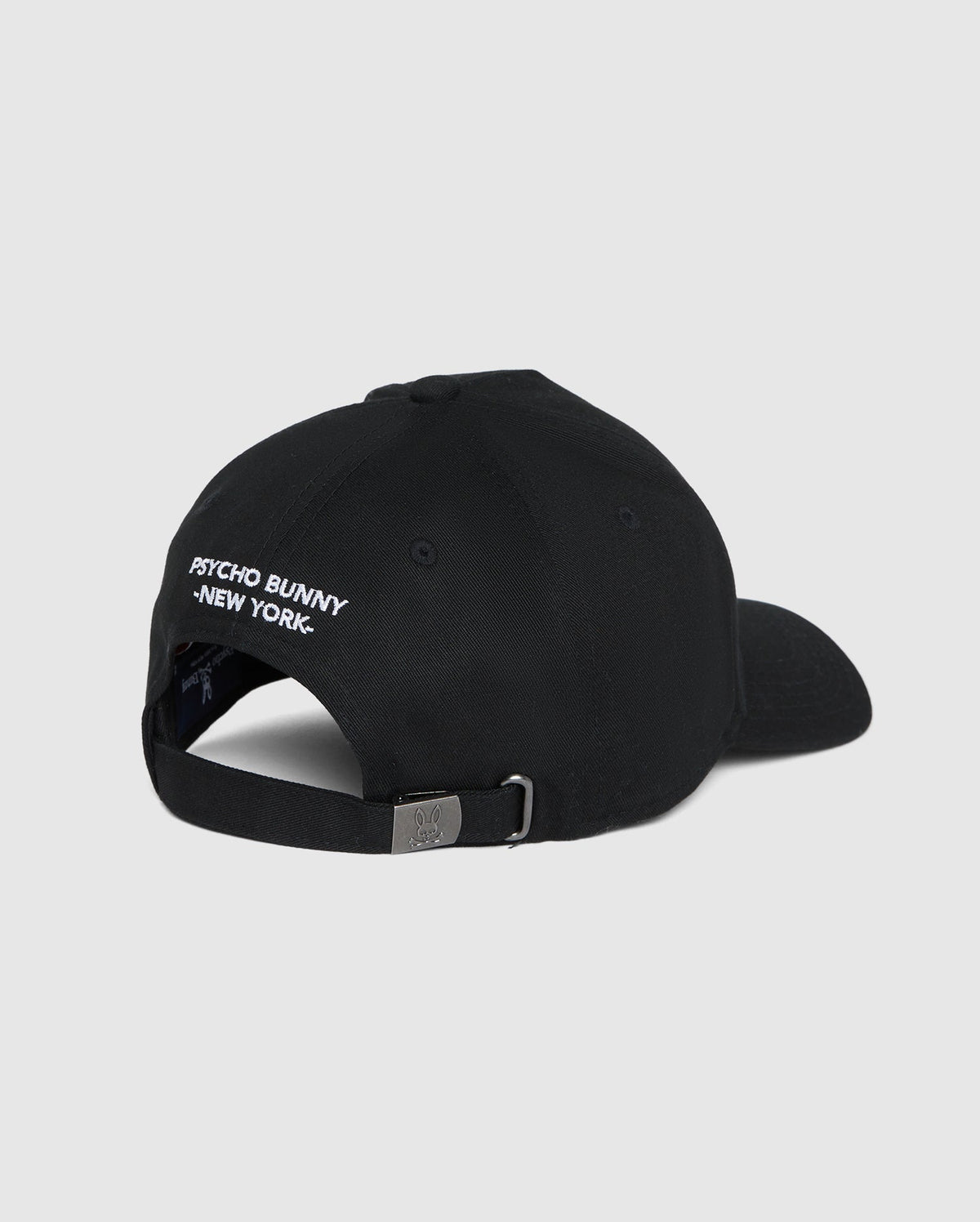Back view of the men's Kingwood embroidered baseball cap (B6A916Y1HT) by Psycho Bunny in black, featuring white embroidered text that reads "PSYCHO BUNNY NEW YORK" above the adjustable backstrap. The cap has a metal buckle on the strap for size adjustment. Plain grey background.