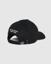 Back view of the men's Kingwood embroidered baseball cap (B6A916Y1HT) by Psycho Bunny in black, featuring white embroidered text that reads "PSYCHO BUNNY NEW YORK" above the adjustable backstrap. The cap has a metal buckle on the strap for size adjustment. Plain grey background.