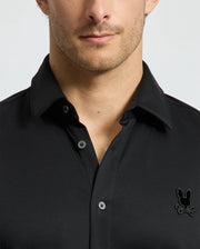 A man dons a stylish MENS INTERLOCK KNIT SHIRT - B6C188E200 by Psycho Bunny, crafted from 100% Pima Cotton, with a subtle rabbit skull logo on the chest. The photo is cropped at the shoulders, obscuring his full face, set against a simple light background.
