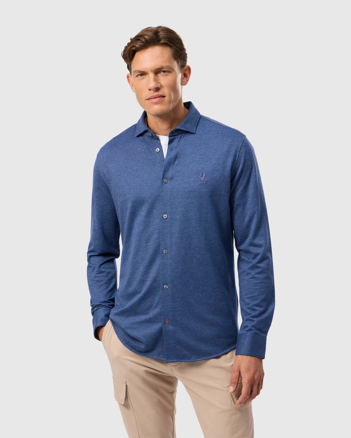 A person wearing a Psycho Bunny MENS DALTON KNIT SHIRT and beige pants stands against a light gray background.