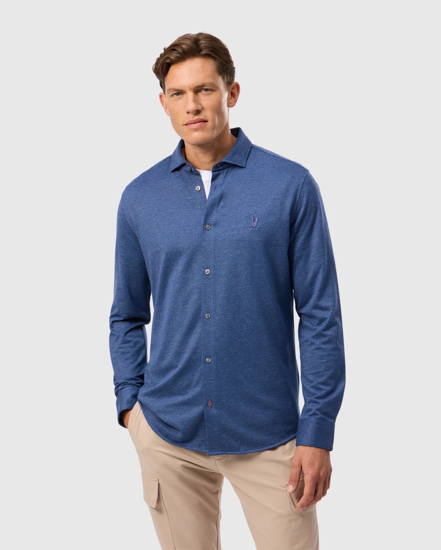 A person wearing a Psycho Bunny MENS DALTON KNIT SHIRT and beige pants stands against a light gray background.