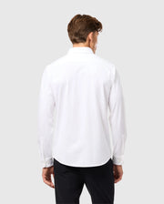 A man with brown hair is facing away, wearing a Psycho Bunny MENS ARTHUR JERSEY SHIRT - B6C748D200 crafted from stretch Pima cotton, paired with black pants against a light gray background.