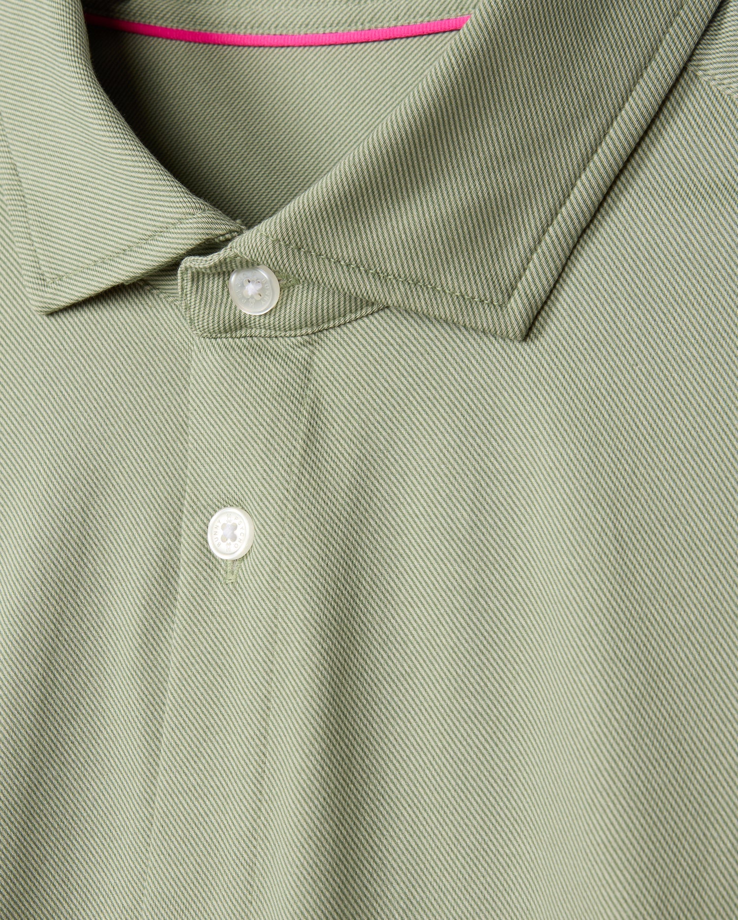 The product is a close-up of the Psycho Bunny MENS BRENDAN JERSEY SHIRT - B6C749D200, featuring a green color with white buttons, made from Pima cotton jersey. It showcases a textured pattern with a neatly folded collar and contrast piping at the inside neckline for added flair.