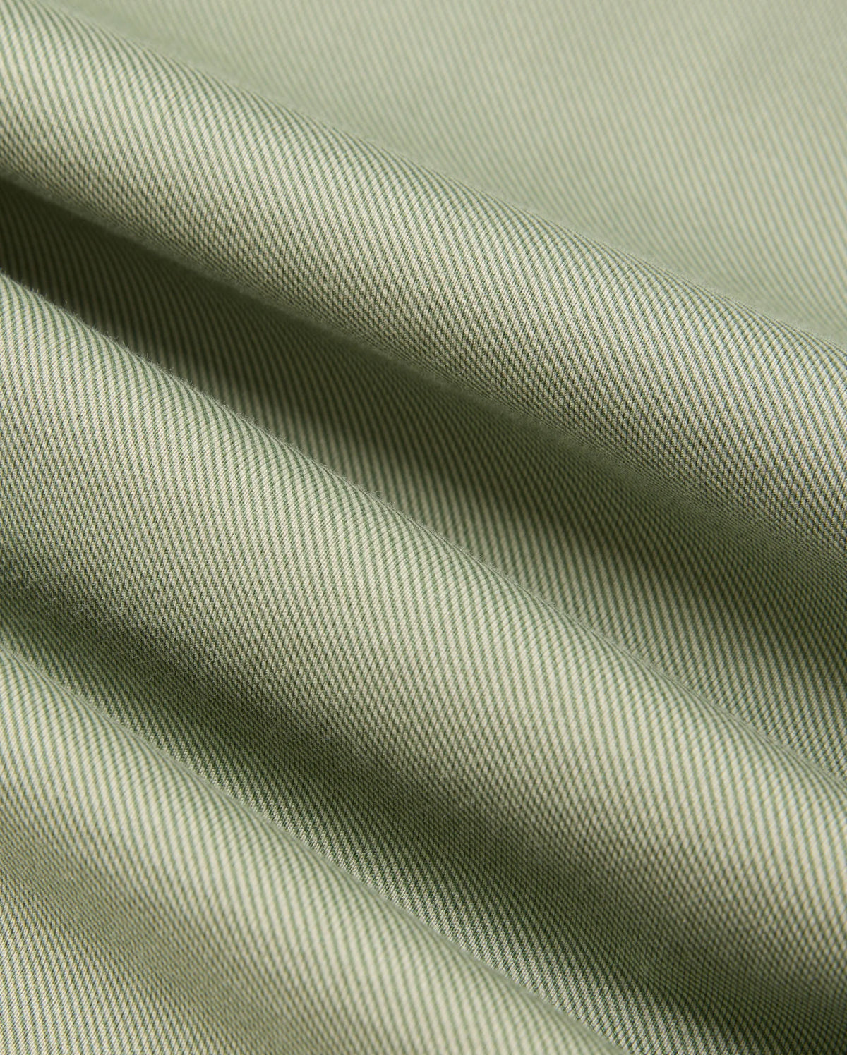 Close-up of the Psycho Bunny MENS BRENDAN JERSEY SHIRT - B6C749D200, featuring a green-striped Pima cotton fabric that displays fine diagonal lines and gentle folds. The material showcases a textured pattern with a smooth appearance, offering a subtle interplay of light and shadow.