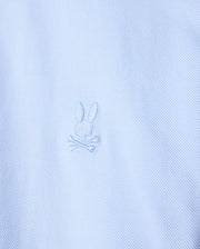 Close-up of the light blue stretch jersey fabric of the Psycho Bunny MENS BRENDAN JERSEY SHIRT - B6C749D200, highlighting the embroidered chest Bunny logo featuring a rabbit head with crossed bones beneath it. The design is subtle, with the logo in a slightly darker shade of blue than the Pima cotton fabric.