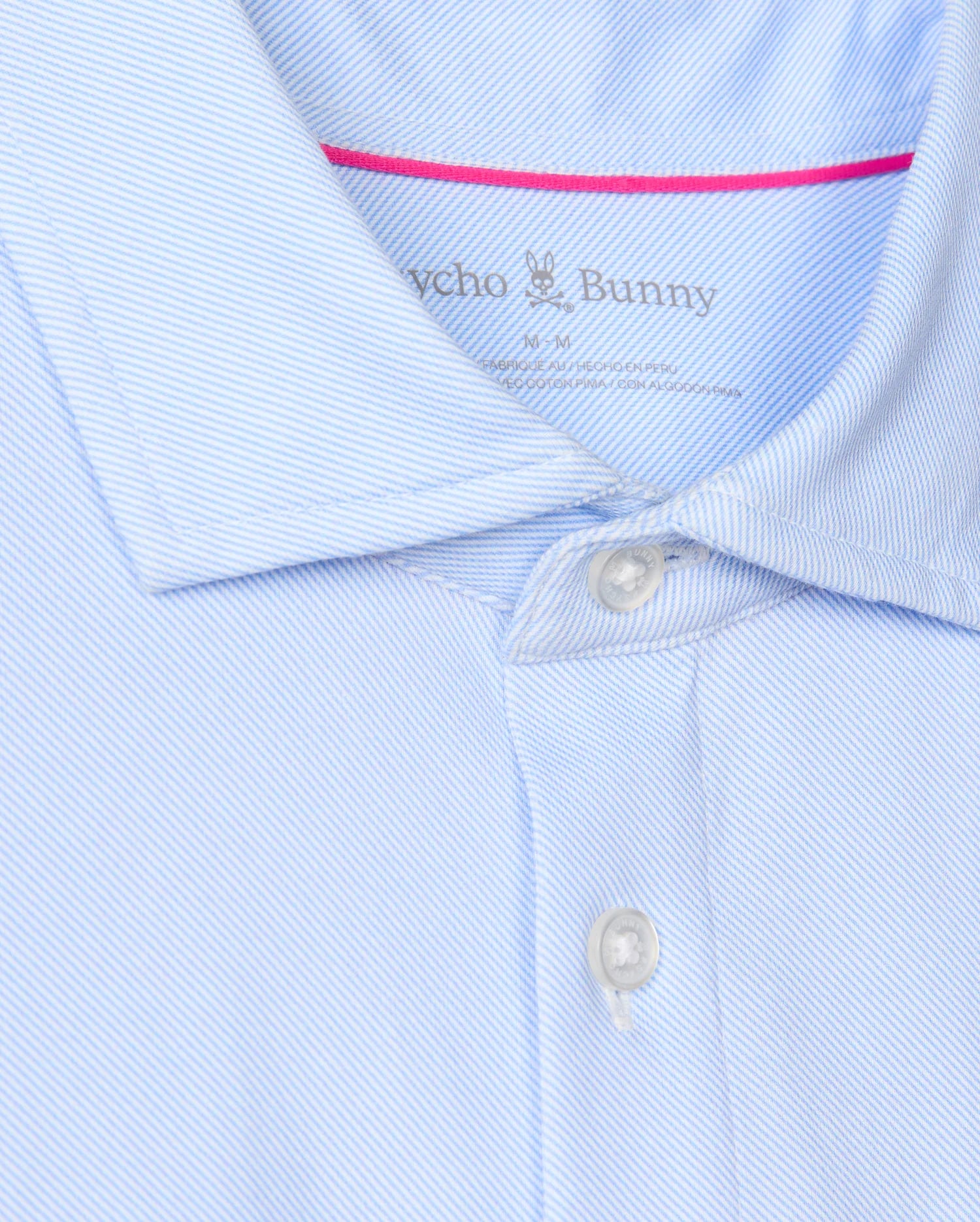 Close-up of the MENS BRENDAN JERSEY SHIRT - B6C749D200 from Psycho Bunny, a light blue button-up shirt in Pima cotton featuring thin white stripes. The image highlights a partial collar with two buttons fastened and displays the "Psycho Bunny" label along with its signature embroidered chest Bunny logo.