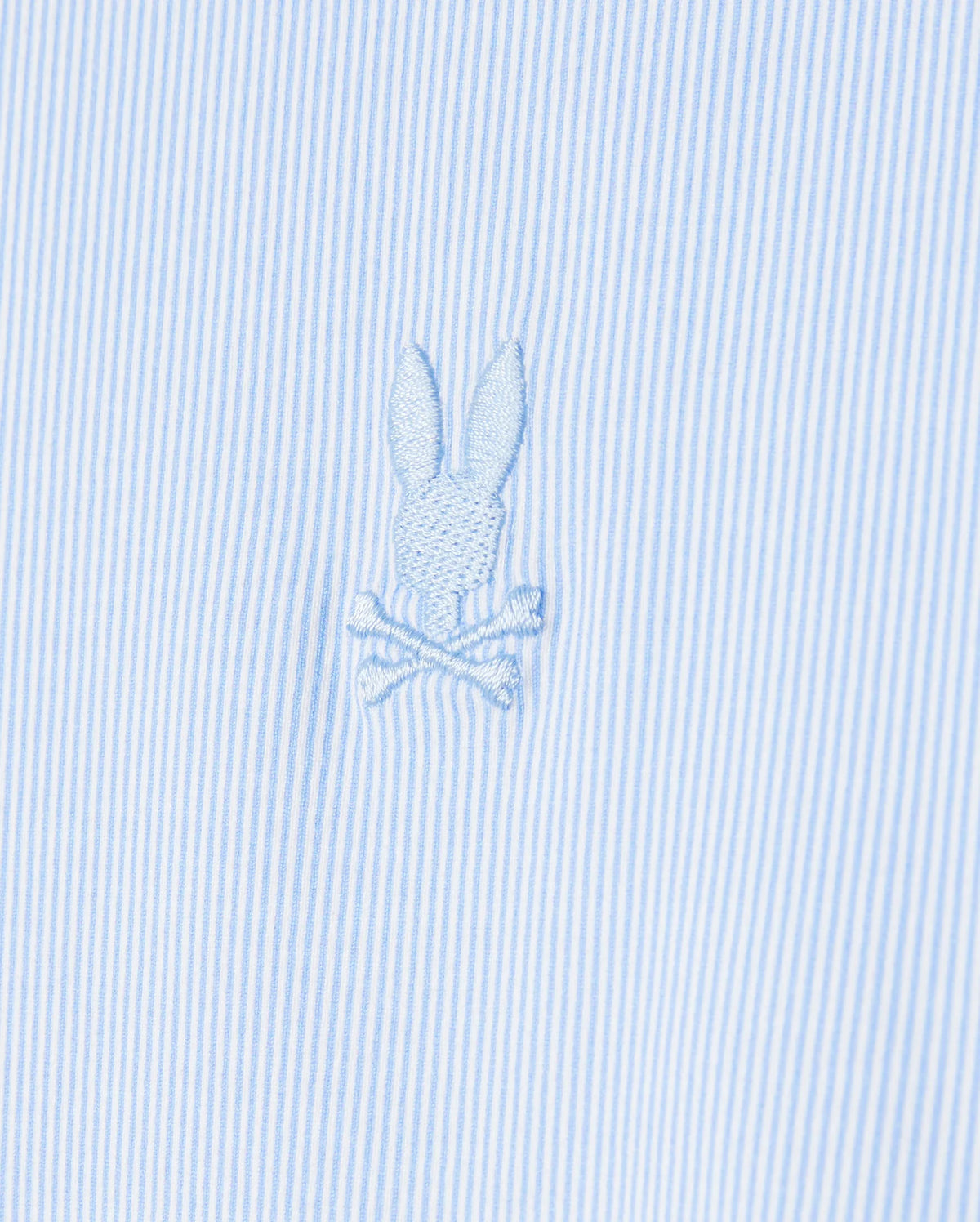 Close-up of the Psycho Bunny men's Brook striped jersey shirt in light blue and white, made from soft Pima cotton and featuring an embroidered emblem of a bunny head above crossed bones.