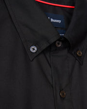 Close-up of the MENS JARED COTTON MODAL SHIRT - B6C774D200 by Psycho Bunny, featuring brown buttons on a premium black fabric. A blue label is sewn inside the collar. A red rod is visible behind the shirt.