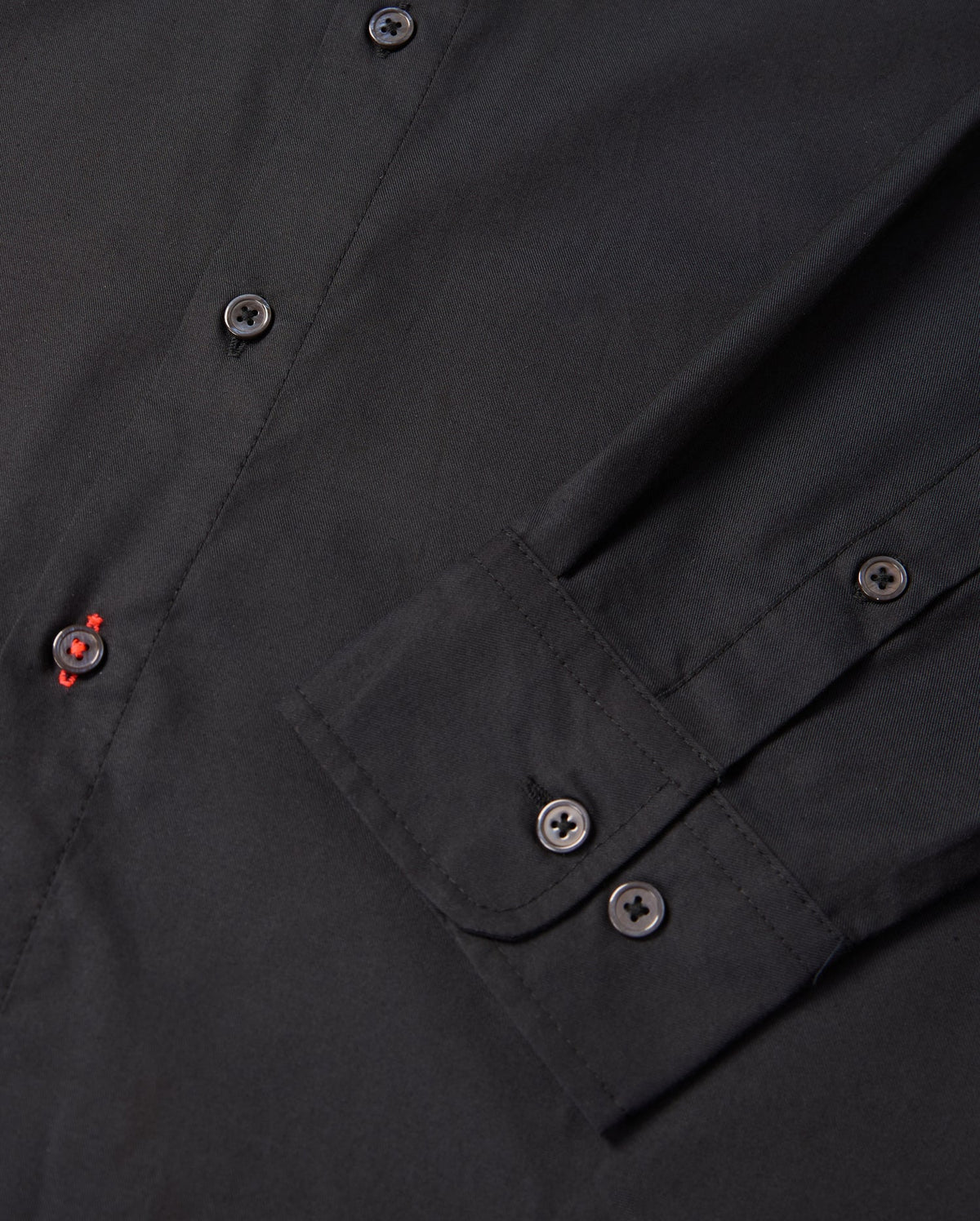 Close-up of the Psycho Bunny MENS JARED COTTON MODAL SHIRT (B6C774D200), featuring a sleeve and front buttons. A red-stitched buttonhole adds contrast to its solid black color, highlighting the refined detail of this elegant piece.