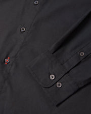Close-up of the Psycho Bunny MENS JARED COTTON MODAL SHIRT (B6C774D200), featuring a sleeve and front buttons. A red-stitched buttonhole adds contrast to its solid black color, highlighting the refined detail of this elegant piece.