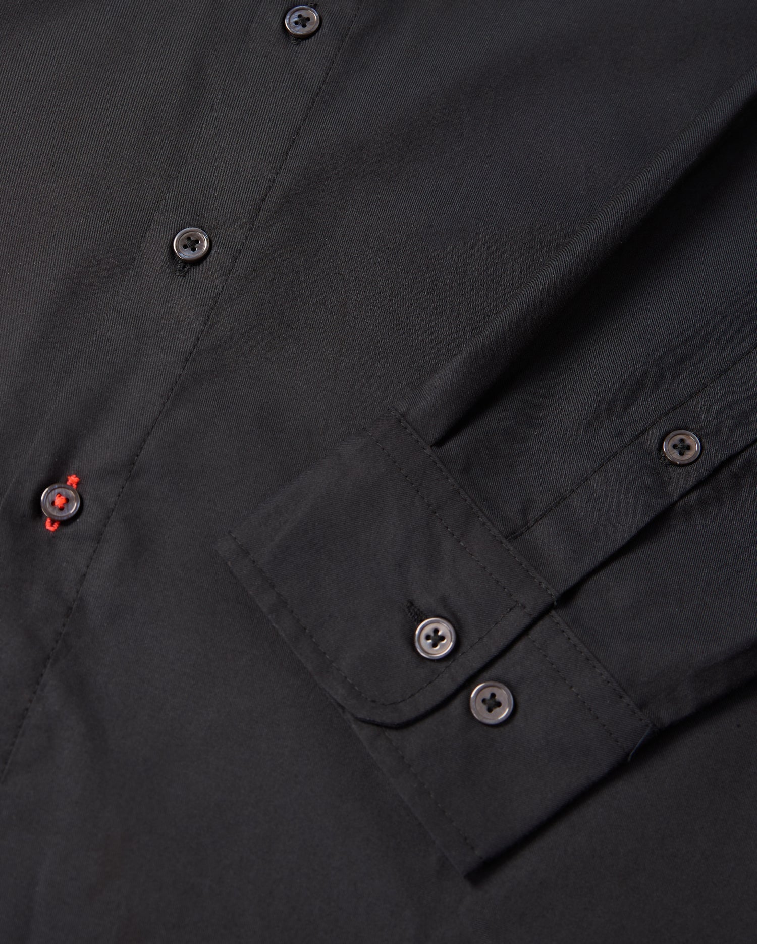 Close-up of the Psycho Bunny MENS JARED COTTON MODAL SHIRT (B6C774D200), featuring a sleeve and front buttons. A red-stitched buttonhole adds contrast to its solid black color, highlighting the refined detail of this elegant piece.