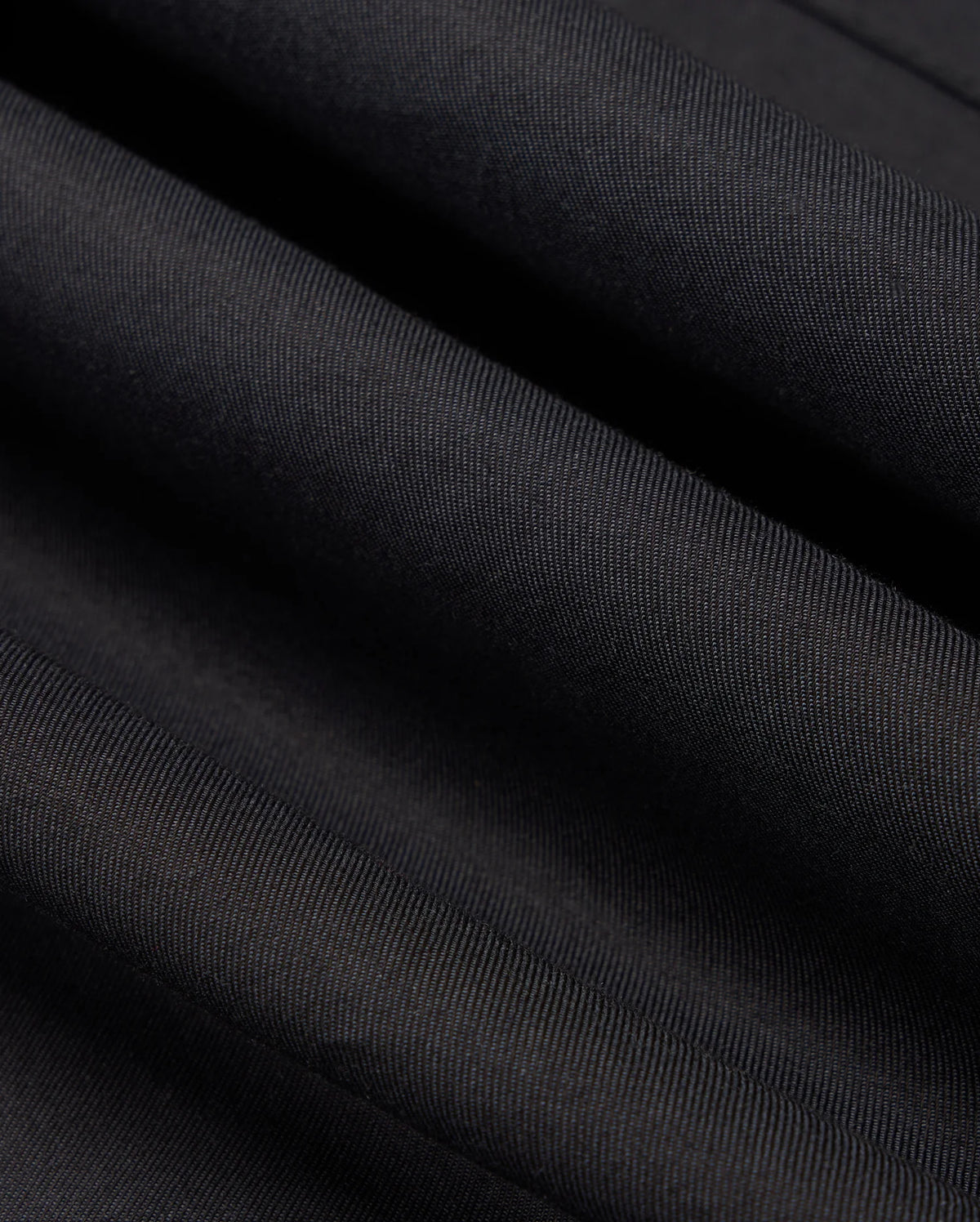 A close-up of Psycho Bunny's MENS JARED COTTON MODAL SHIRT in dark gray or black highlights a premium cotton fabric with subtle diagonal textures, folded slightly to create gentle waves and shadows, ideal for crafting its smooth and soft appearance.