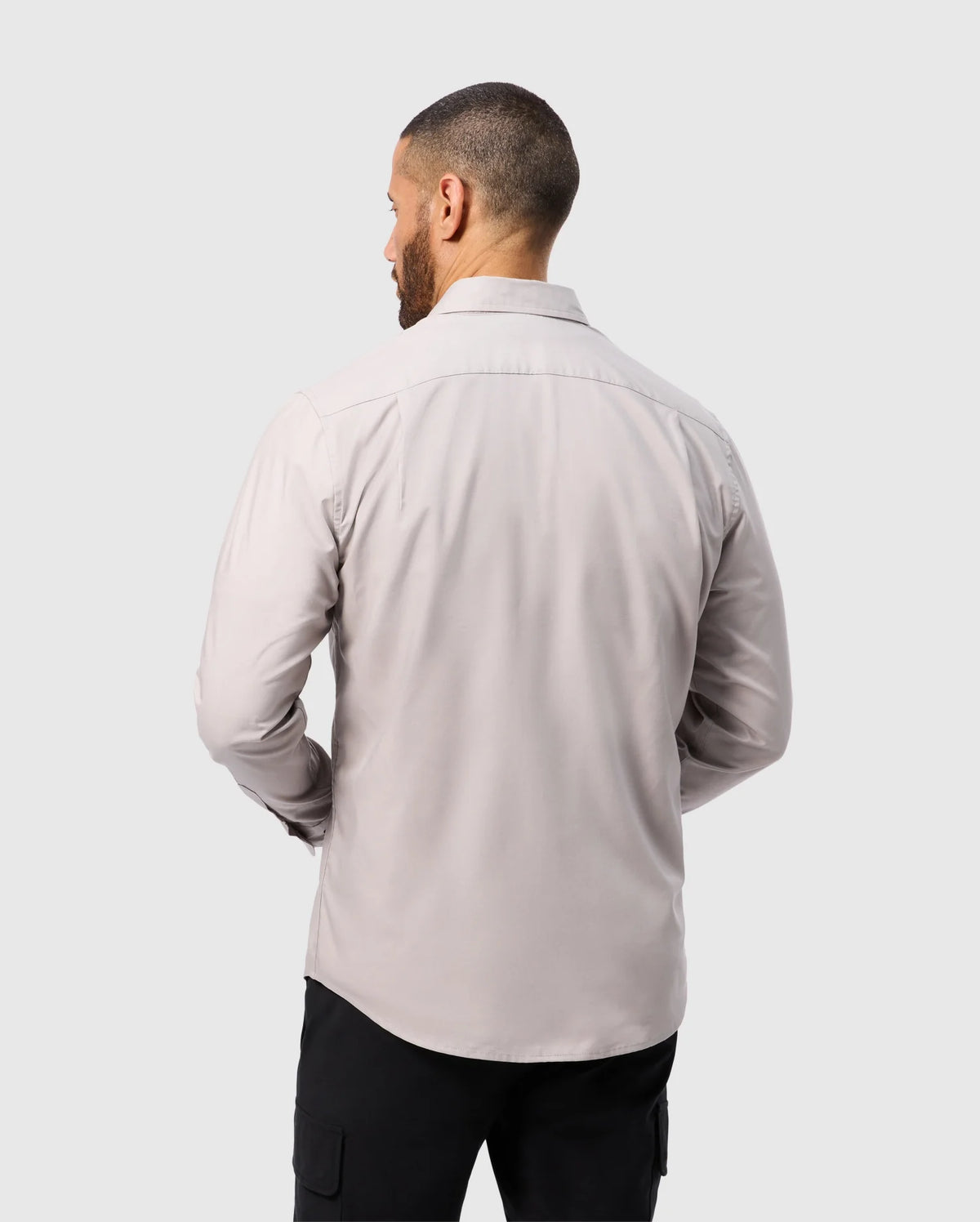 A man with short hair is seen from behind in a light gray Psycho Bunny MENS JARED COTTON MODAL SHIRT (B6C774D200) paired with black cargo pants against a neutral background.