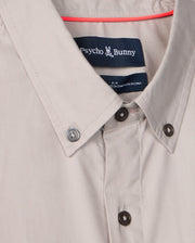 Close-up of the men's Jared cotton modal shirt by Psycho Bunny, featuring a label with the iconic bunny logo. Crafted in a soft beige pima cotton modal blend, it blends style and comfort seamlessly.