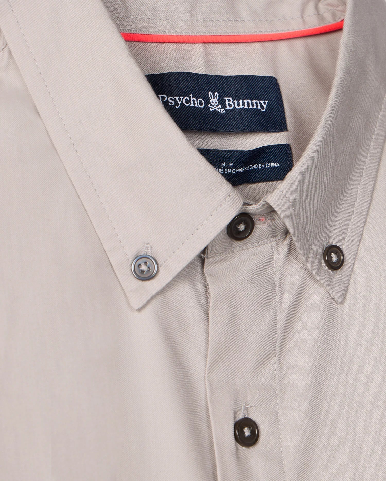 Close-up of the men's Jared cotton modal shirt by Psycho Bunny, featuring a label with the iconic bunny logo. Crafted in a soft beige pima cotton modal blend, it blends style and comfort seamlessly.