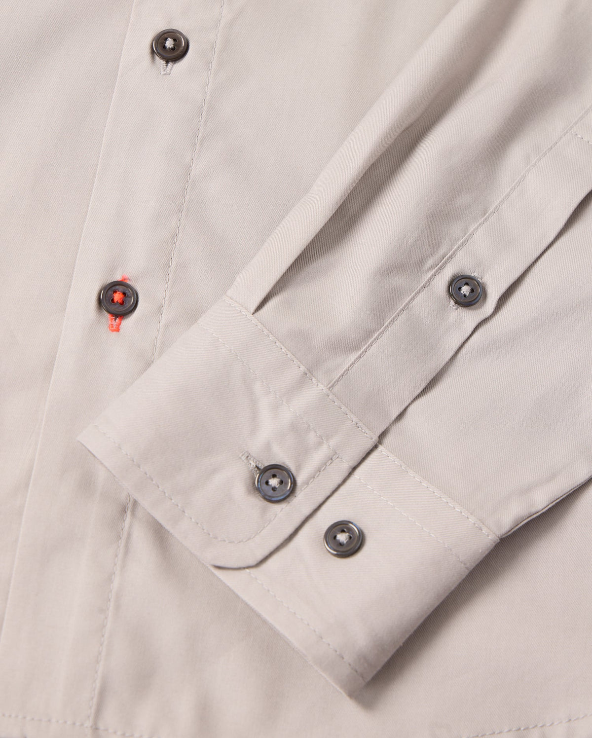 Close-up of the MENS JARED COTTON MODAL SHIRT by Psycho Bunny, showing its beige cuff with grey buttons and folded sleeve. Red thread on one buttonhole adds contrast, highlighting the detailed stitching of this premium shirt.