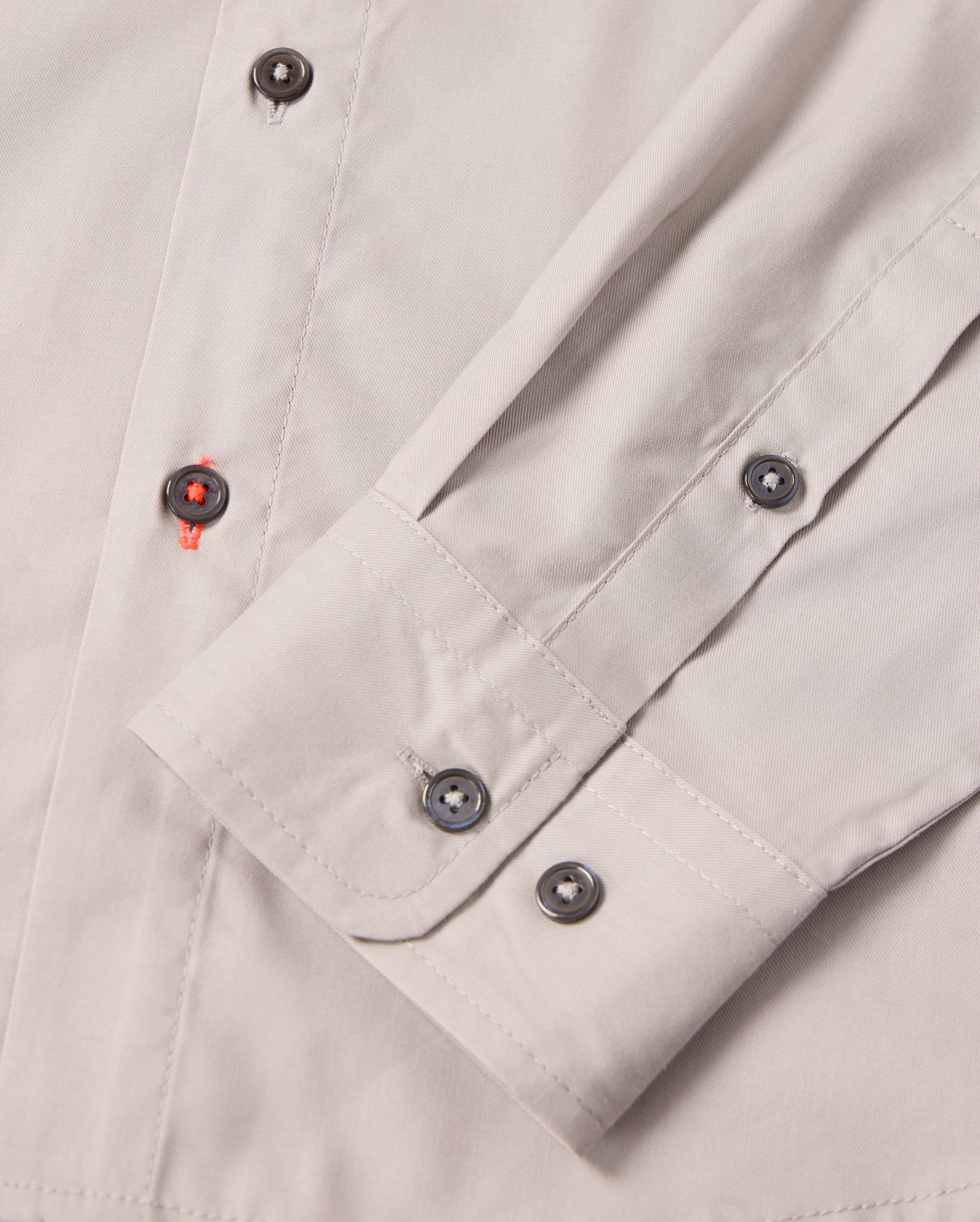 Close-up of the MENS JARED COTTON MODAL SHIRT by Psycho Bunny, showing its beige cuff with grey buttons and folded sleeve. Red thread on one buttonhole adds contrast, highlighting the detailed stitching of this premium shirt.