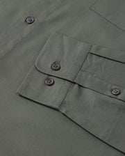 Close-up of a green fabric with a flap pocket and four black buttons from the Psycho Bunny MENS JARED COTTON MODAL SHIRT. The premium cotton modal fabric appears smooth and neatly stitched, showcasing a visible part of this men's garment.