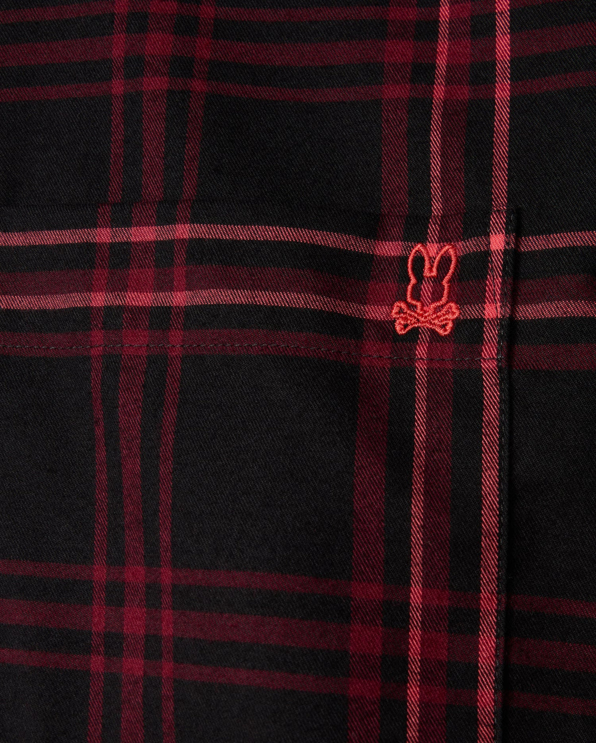 Close-up of the MENS HAYES PLAID SHIRT - B6C842D200 by Psycho Bunny, a black and red plaid shirt crafted from soft Pima cotton, featuring a small embroidered design with a playful bunny ears and crossbones motif in red.