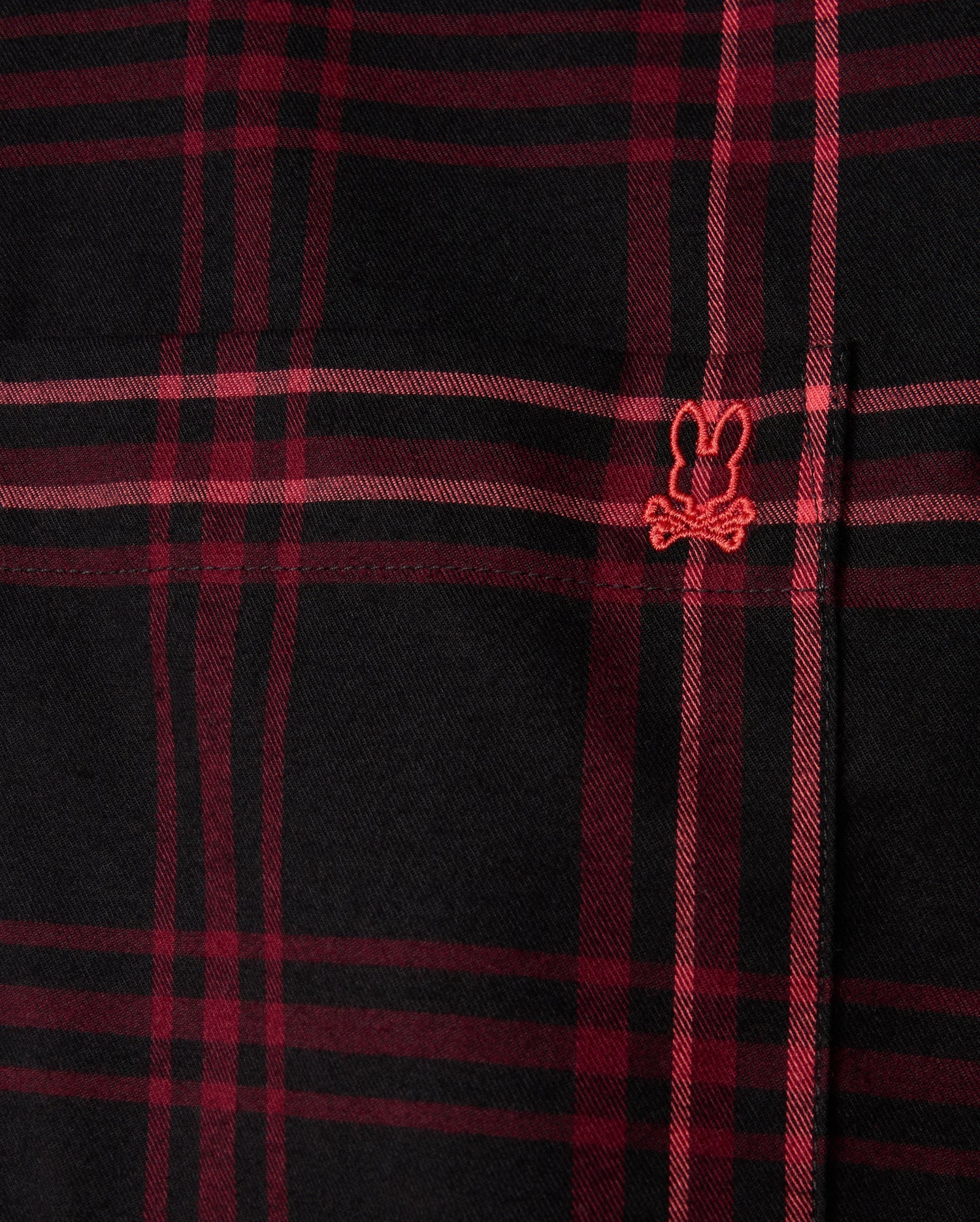 Close-up of the MENS HAYES PLAID SHIRT - B6C842D200 by Psycho Bunny, a black and red plaid shirt crafted from soft Pima cotton, featuring a small embroidered design with a playful bunny ears and crossbones motif in red.