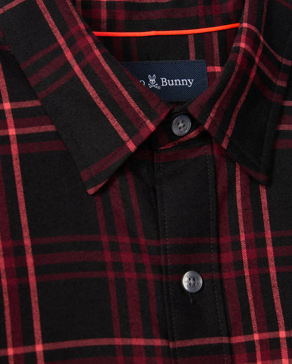 A close-up of the Psycho Bunny MENS HAYES PLAID SHIRT (B6C842D200) showcases its red and black button-down plaid pattern, complemented by a folded collar and visible buttons. Crafted from soft Pima cotton, the shirt includes a small logo label with partially visible text sewn inside the neckline.
