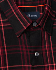 A close-up of the Psycho Bunny MENS HAYES PLAID SHIRT (B6C842D200) showcases its red and black button-down plaid pattern, complemented by a folded collar and visible buttons. Crafted from soft Pima cotton, the shirt includes a small logo label with partially visible text sewn inside the neckline.