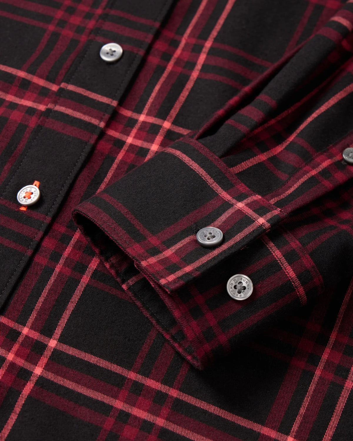 Close-up of the MENS HAYES PLAID SHIRT (B6C842D200) by Psycho Bunny in black and red, showcasing a folded sleeve with two buttoned cuffs. The fabric features a classic tartan pattern with intersecting lines and offers a smooth texture due to its Pima cotton construction.