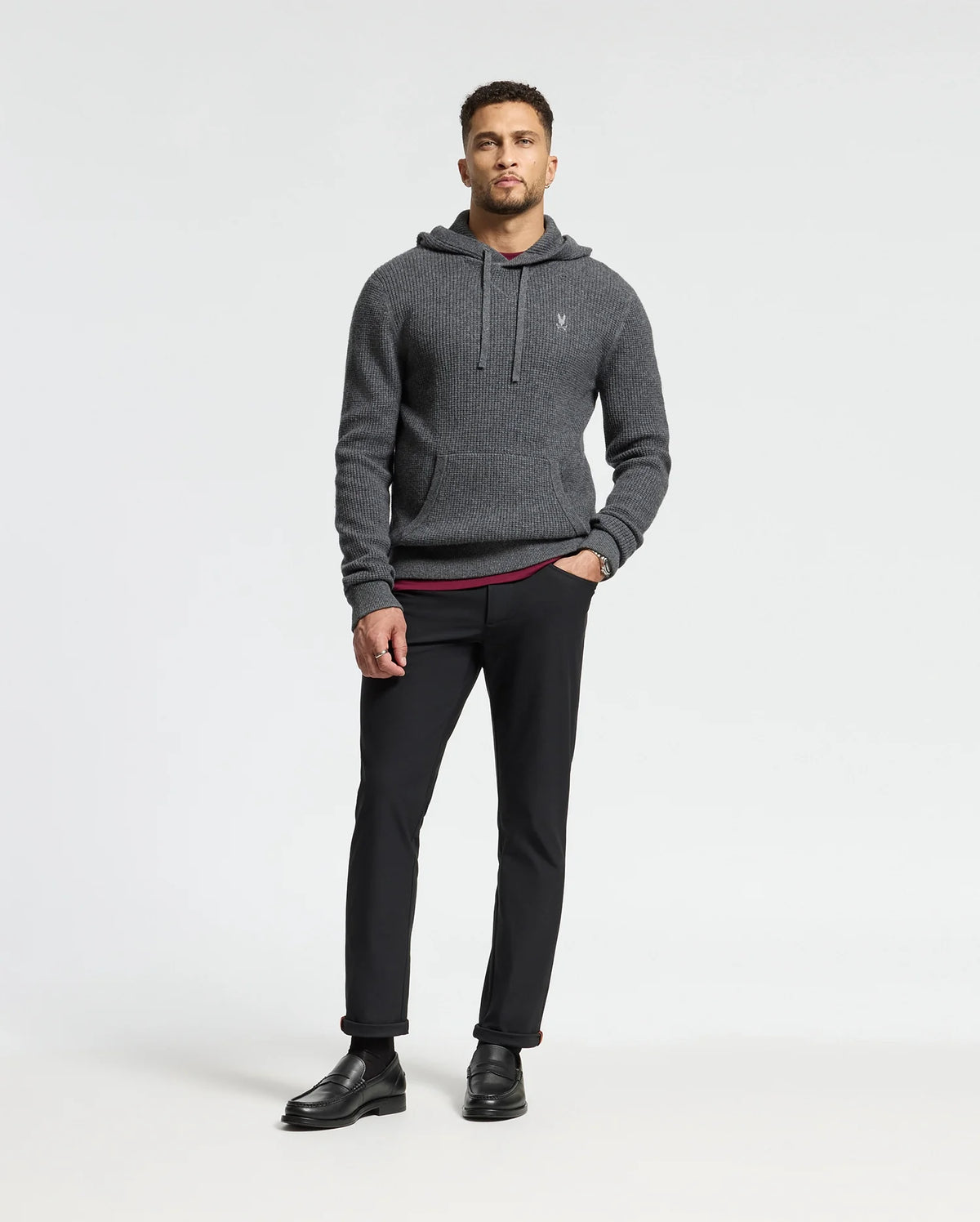 A man in a Psycho Bunny dark gray MENS LEVAN WAFFLE HOODED SWEATER, black pants, and shoes stands against a plain white background. He has short hair and is looking directly at the camera.