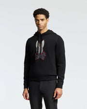 A person is wearing the Psycho Bunny MENS BULDER HOODED SWEATER - B6E261E200, crafted from supple Supima cotton and featuring a large white and red stylized rabbit design on the front. This hoodie is perfectly paired with black pants against a plain white background.
