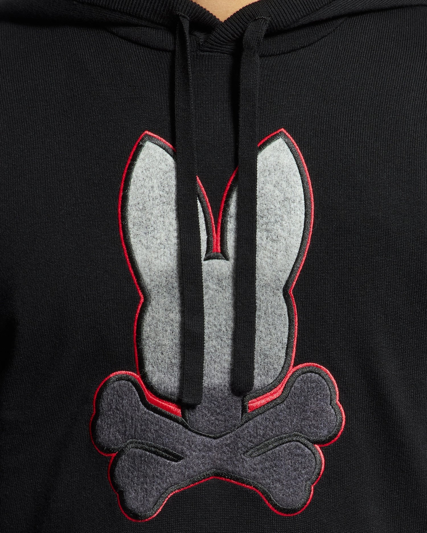 The MENS BULDER HOODED SWEATER - B6E261E200 by Psycho Bunny boasts a striking design featuring a large gray and red outlined bunny head above crossed bones. Made from soft Supima cotton, it includes front-hanging drawstrings that enhance its sleek appearance.