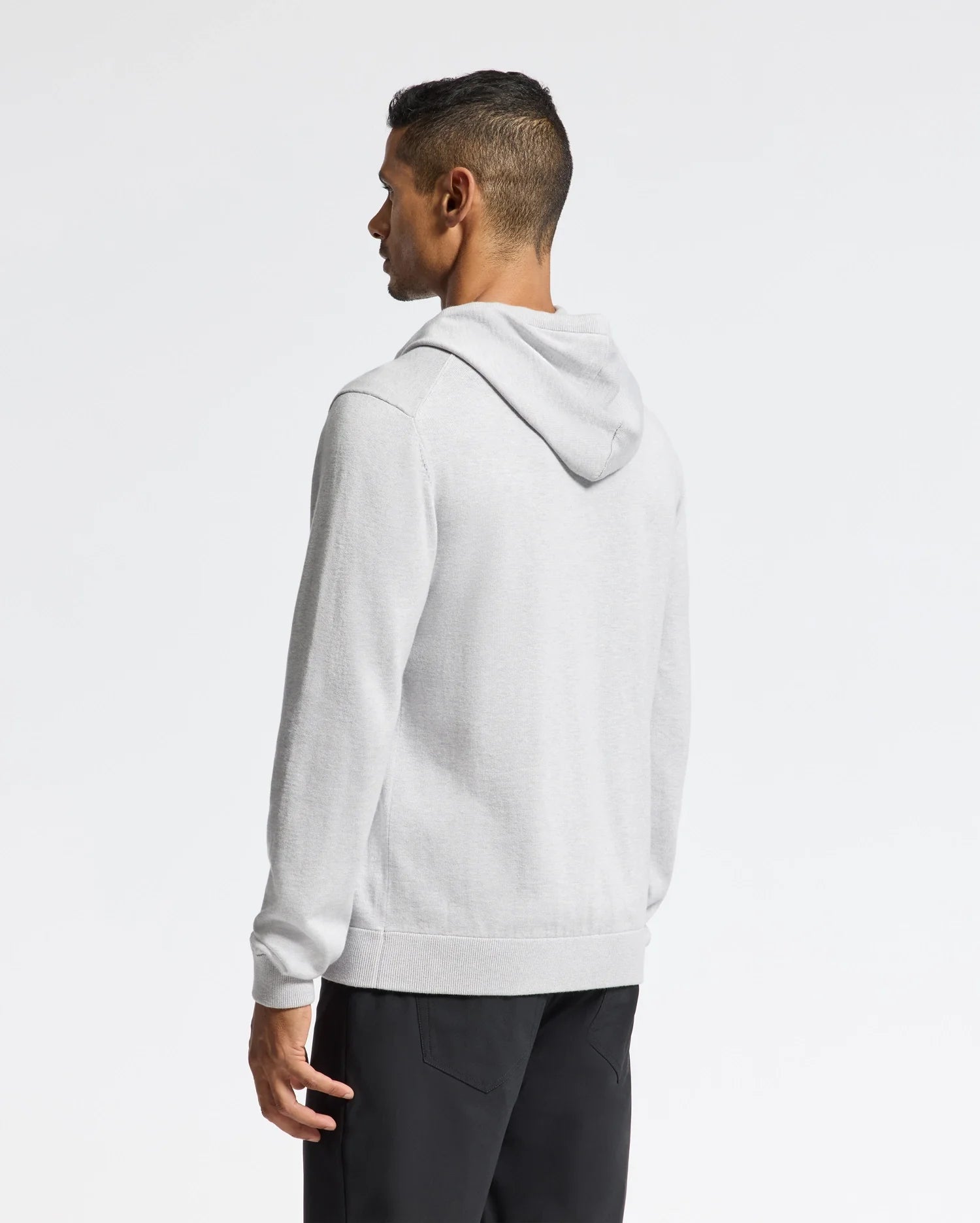 A person facing away wears a Psycho Bunny MENS BULDER HOODED SWEATER in gray, paired with black pants. The background is plain white, and the person's hair is dark and short.