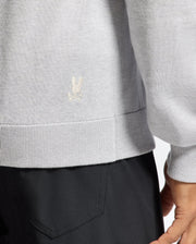 A person wears a Psycho Bunny MENS BULDER HOODED SWEATER - B6E261E200 in light gray, featuring a small embroidered logo on the hem. Paired with dark pants, the image focuses on clothing details with the person partially cropped out.