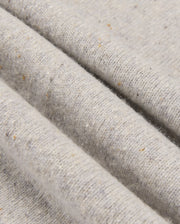 A close-up of the MENS LINCOLN MERINO WOOL SWEATER - B6E831D200 by Psycho Bunny highlights its textured merino wool fabric in light gray, adorned with subtle speckles of brown and beige. This soft, slightly ribbed surface creates gentle folds and shadows, showcasing a timeless style.