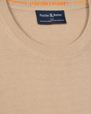 A close-up of the MENS BELMORE EXTRA FINE COTTON SWEATER - B6E832D200 by Psycho Bunny shows its beige fabric, ribbed neckline, and tag with brand details. The inner collar displays "PSYCHO BUNNY" in vibrant orange, and a tonal embroidered Bunny logo adds subtle elegance.