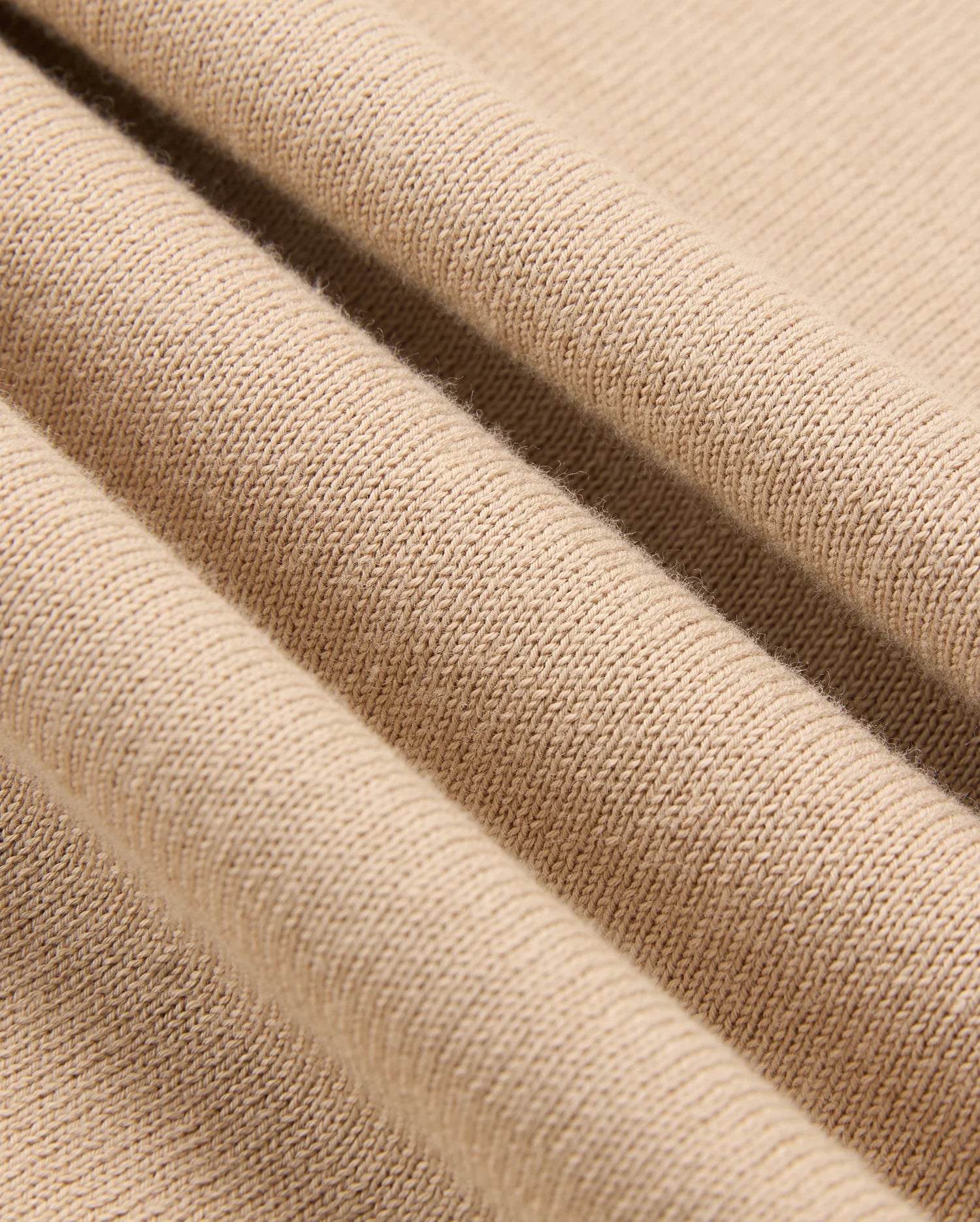 Close-up image of beige knitted fabric from the Psycho Bunny Men's Belmore Extra Fine Cotton Sweater (B6E832D200), showcasing detailed texture and folds. The uniform pattern highlights the material's softness and elasticity.