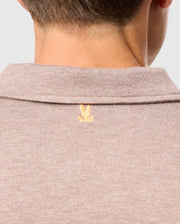 Close-up of the back of a person's neck wearing the luxury MENS BRADSHAW POLO SWEATER in beige, crafted by Psycho Bunny from premium men's Merino wool. It features a small embroidered yellow logo resembling a bird with open wings at the top center of the collar.