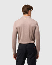 A person with short brown hair stands back to the camera, wearing a Psycho Bunny MENS BRADSHAW POLO SWEATER in light brown paired with black pants. The plain, light gray backdrop accentuates the elegance of this luxurious merino wool attire.