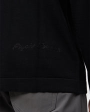 Close-up of a person wearing the Psycho Bunny MENS CORY CHAINSTITCH COTTON SWEATER - B6E893D200 in black, showcasing subtle chainstitch embroidery on the side. The lower half of the sweater is visible, paired with gray pants that have prominent stitching on the pockets.