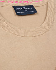 Close-up of a beige MENS CORY CHAINSTITCH COTTON SWEATER - B6E893D200 by Psycho Bunny, featuring a round neckline. The brand name "Psycho Bunny" appears in white on a dark tag, while "PSYCHO BUNNY" is crafted in pink chainstitch embroidery above the label, showcasing the expert craftsmanship of this lightweight cotton sweater.