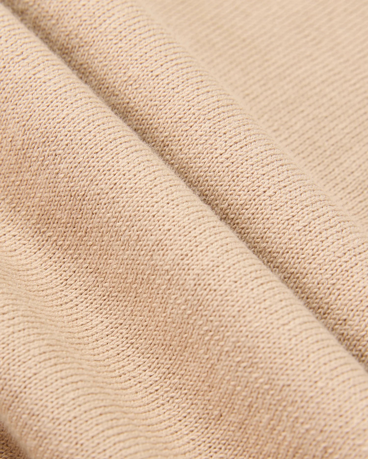 Here's a close-up of the MENS CORY CHAINSTITCH COTTON SWEATER by Psycho Bunny. This beige sweater features a lightweight cotton fabric with a textured, woven pattern, draped in gentle folds to highlight its soft and flexible nature.