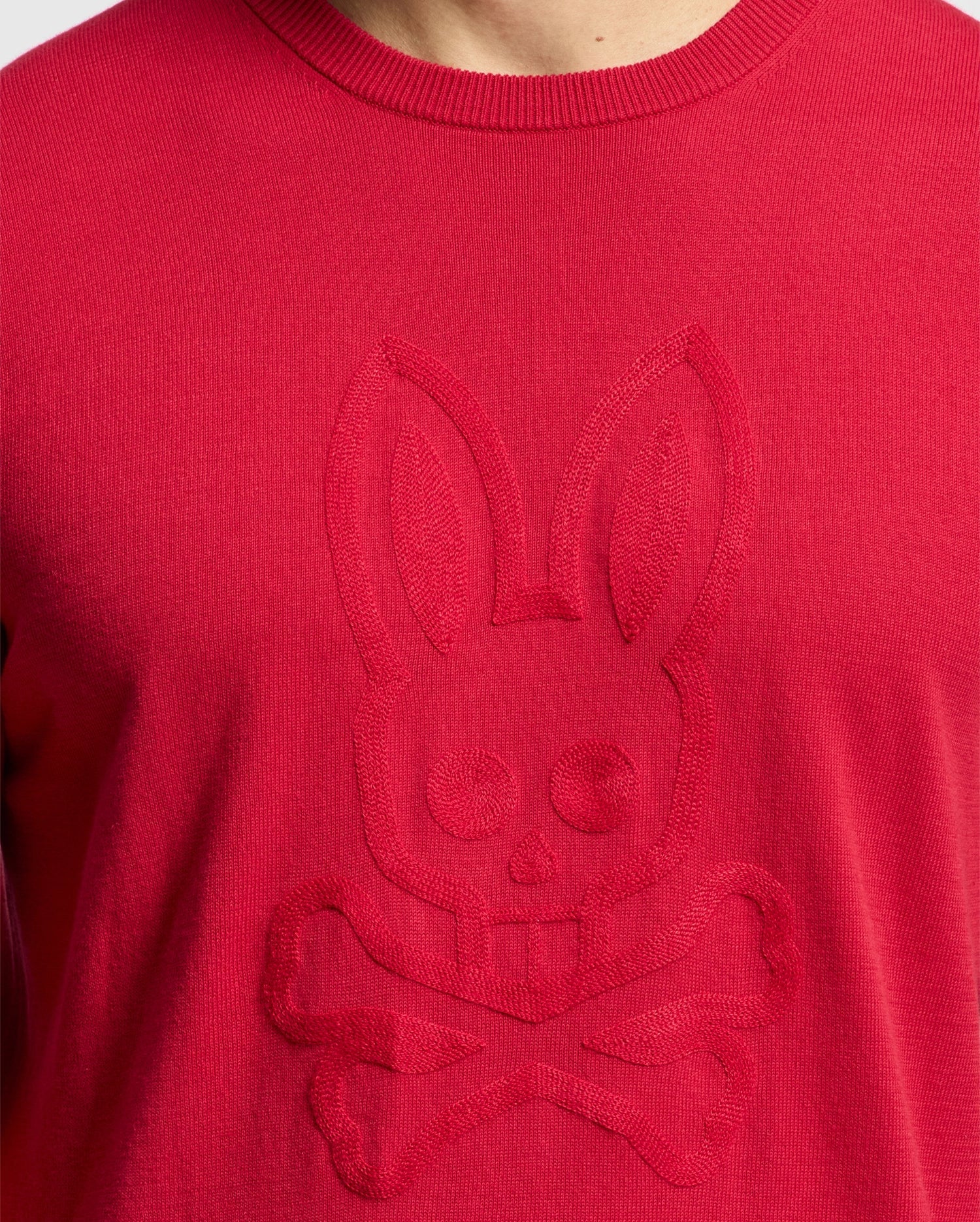 Close-up of a Psycho Bunny MENS COORY CHAINSTITCH COTTON SWEATER in red, showcasing an embossed bunny skull and crossbones design with intricate chainstitch embroidery on the front.