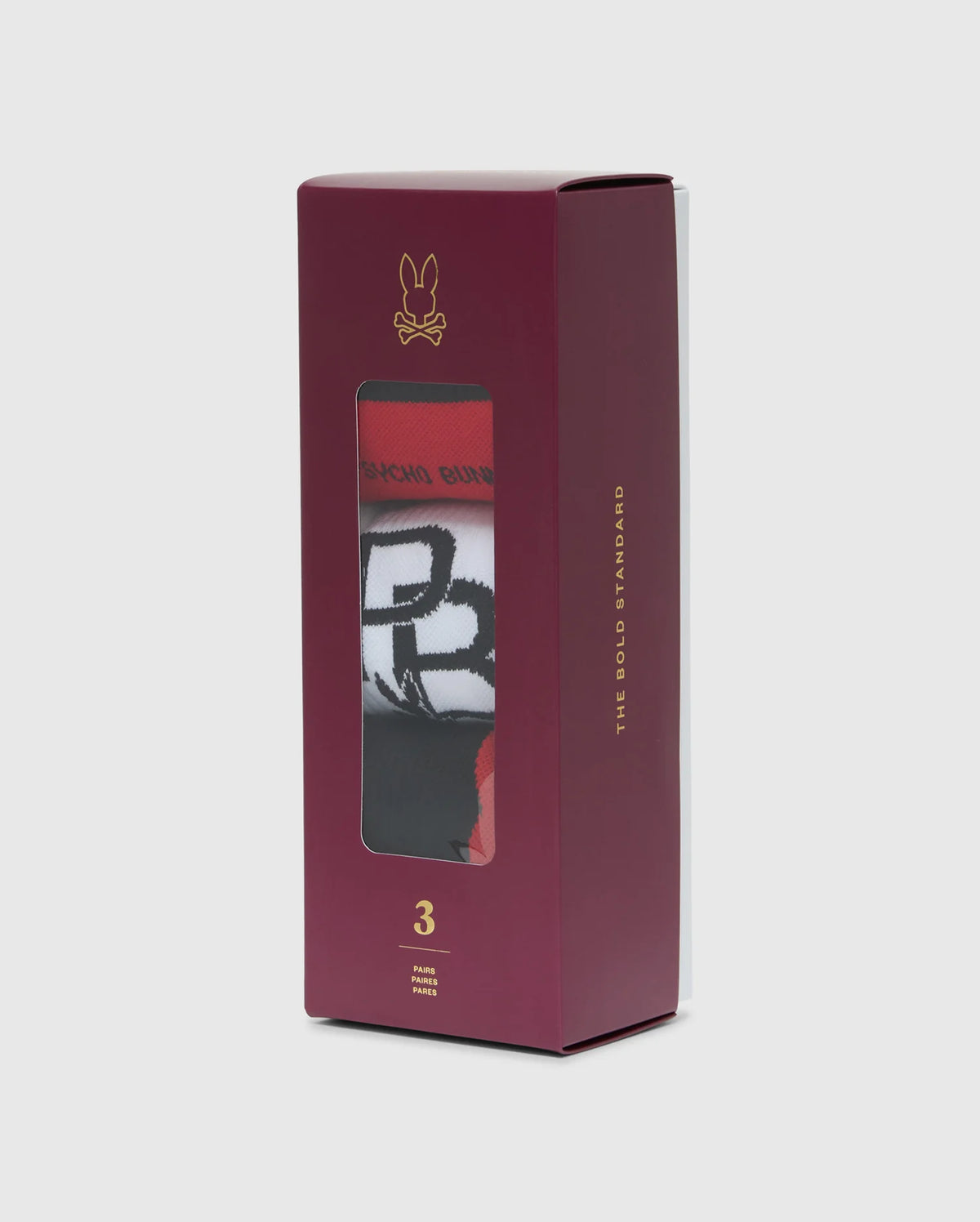 A maroon box containing three pairs of vibrant men's sport socks featuring black and white designs, visible through a transparent window. These socks are made from premium Peruvian Pima cotton and designed with moisture-wicking properties. The box is adorned with a small golden Psycho Bunny logo and the phrases "THE BOLD STANDARD" and "3 PAIRS." The product name is MENS SPORT SOCK BOX SET - B6F268E200.