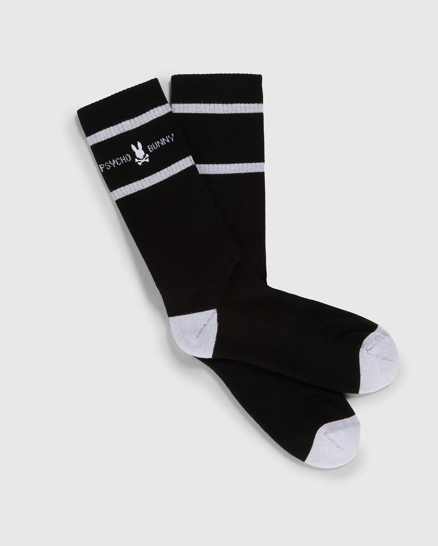 A pair of black knee-high Psycho Bunny fashion socks with white toe and heel patches and two white horizontal stripes near the top, featuring the text "PSYCHO BUNNY" in white.