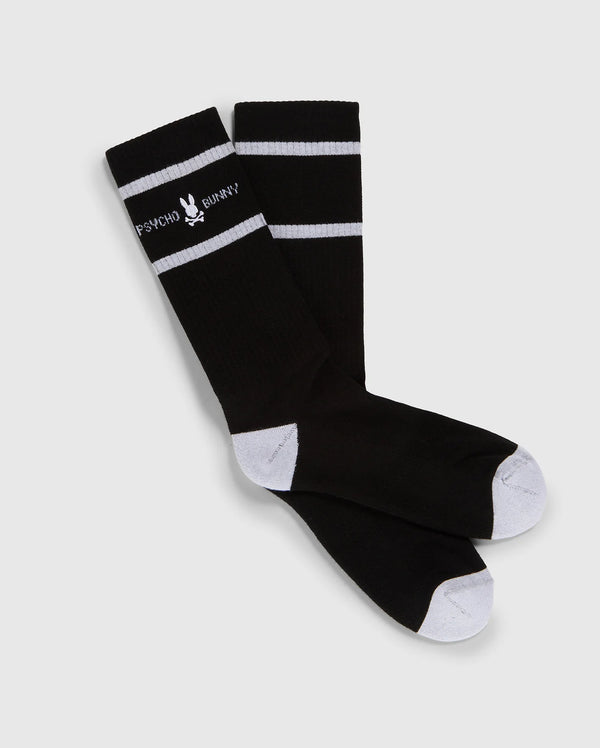 A pair of black knee-high Psycho Bunny fashion socks with white toe and heel patches and two white horizontal stripes near the top, featuring the text "PSYCHO BUNNY" in white.